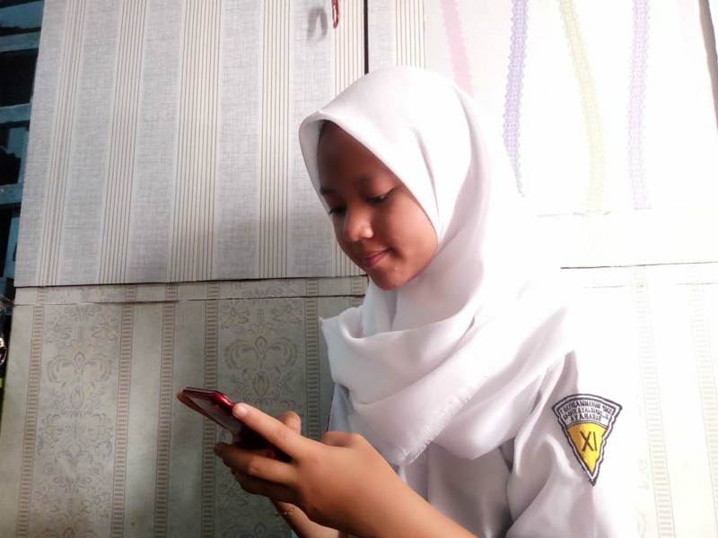 Siswi SMP Mutu Ocha Setiana Dewi mengerjakan ujian online pakai HP. (Rukhan/PWMU.CO)